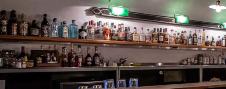 Die Flaschenwand hinter der Theke: zwei Reihen Gin, Whisky und Liköre unter einer grünen Lampe.